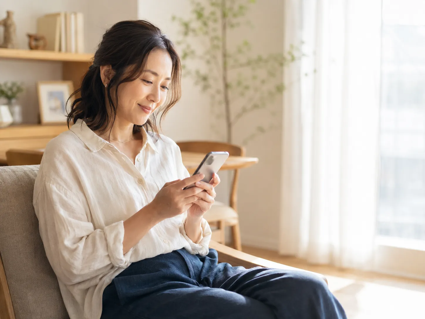 自宅リビングで家族の歩数をスマートフォンで確認し、穏やかに微笑む40代女性