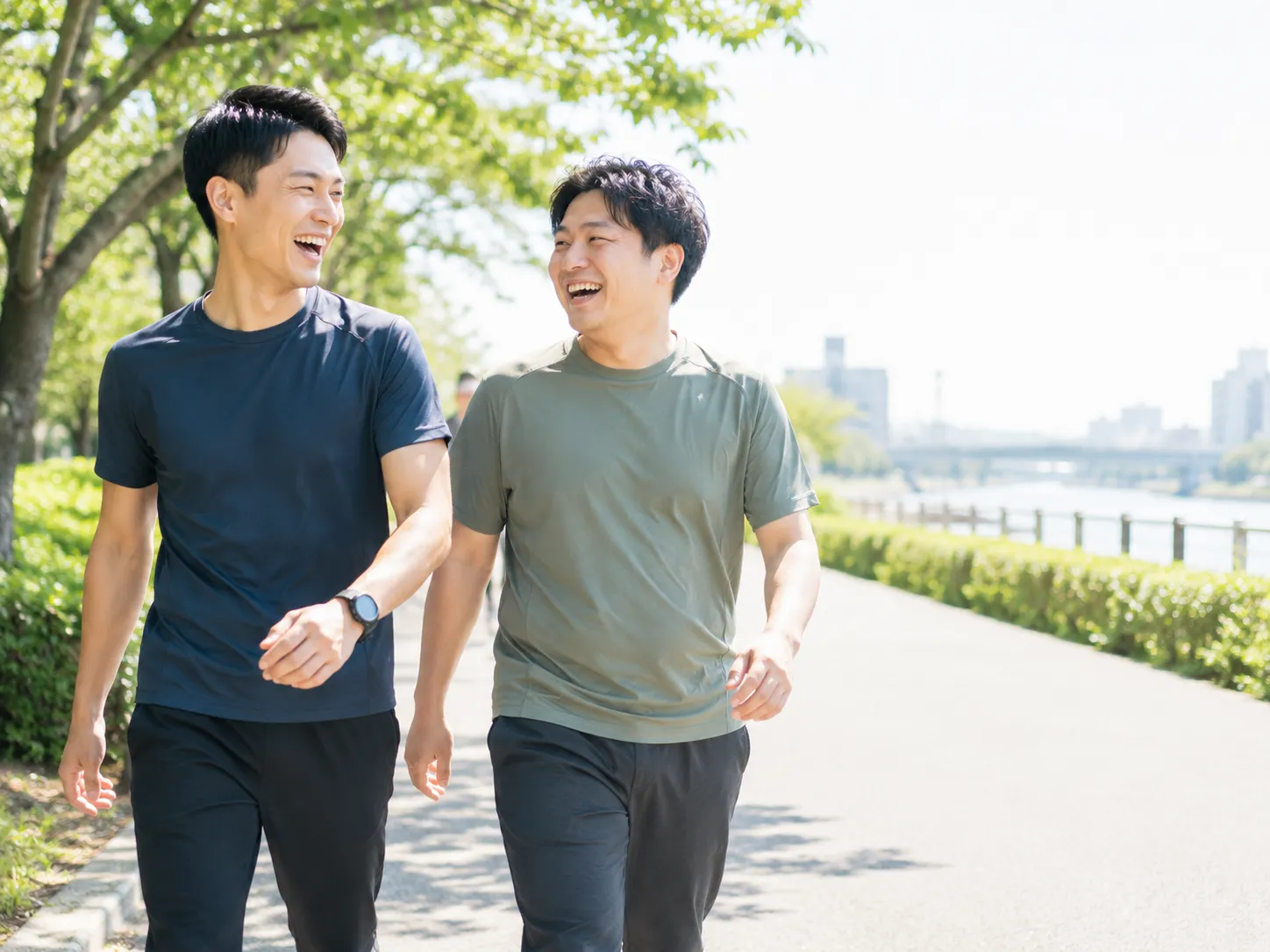 河川敷を笑いながら並んで歩く、励まし合う20-30代の男性2人